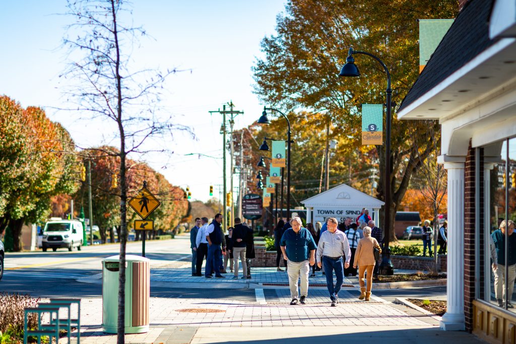 Citizens walk across a new crosswalk in downtown Spindale, surrounded by light posts featuring the Spindale brand.